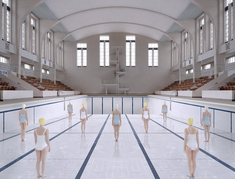 BON ACCORD SWIMMING POOL: An indoor swimming pool with an arched ceiling and large windows is empty except for a group of women in white swimsuits standing in the middle of the pool deck. They all have their backs to the camera, and their heads are turned slightly to the left. The pool is filled with water, but the surface is still and reflective. The white tile walls and floor create a stark and clean environment.