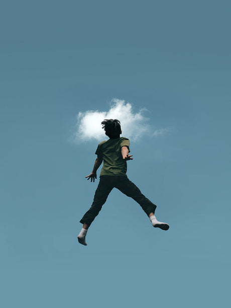 HEAD IN THE CLOUDS: An astronaut wearing a white space suit and a halo stands amongst fluffy white clouds, with large white feathered wings behind them. The astronaut is facing forward, looking straight ahead.