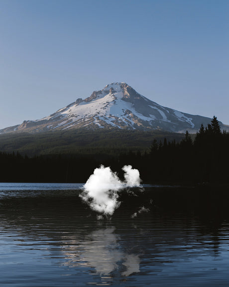 CLOUD DANCE: A serene image showcasing Mount Hood, a majestic, snow-capped volcano in Oregon, reflected in the still waters of a lake. The mountain stands tall and imposing against a clear, blue sky, while the tranquil water reflects its beauty. The scene is tranquil and picturesque, offering a glimpse into the natural beauty of the Pacific Northwest.