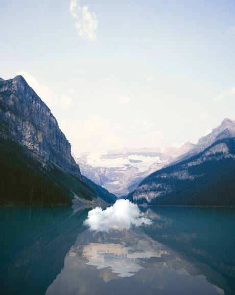 EARTH BREATH: A single, fluffy cloud reflects in the calm waters of Lake Louise, nestled amidst the majestic peaks of Banff National Park. The mountains rise on either side of the lake, creating a breathtaking natural scene.