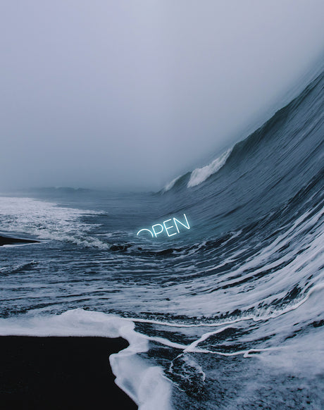 INTRO: A photo of a black sand beach with white foam from the waves crashing on the shore. In the distance, a large wave is about to break. The word OPEN is written in neon lights on the beach.