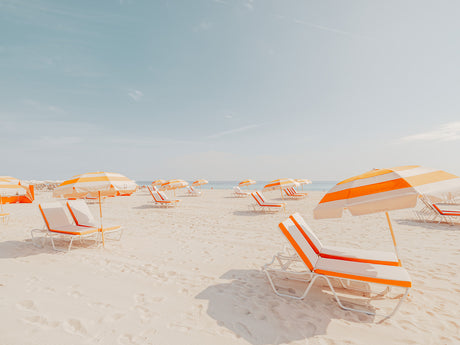 MIAMI BEACH III: A sunny beach scene with white sand, blue skies, and multiple striped umbrellas providing shade for the lounge chairs. There are no people visible, creating a sense of peace and tranquility.