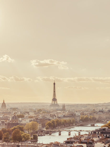 PARIS SKYLINE: A breathtaking view of Paris, France, at sunset. The iconic Eiffel Tower stands tall against the hazy sky, with the citys sprawling cityscape spread out below. The Seine River winds its way through the urban landscape, reflecting the warm light of the setting sun.