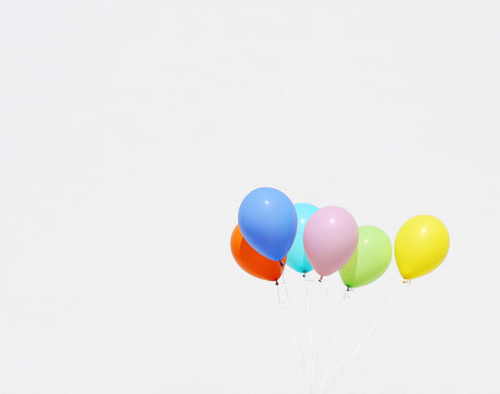 RAINBOW BALLOONS 2: A group of colorful balloons float against a bright white sky. The balloons are blue, orange, pink, green, and yellow. The photo appears to have been taken during the day on a clear, sunny day.