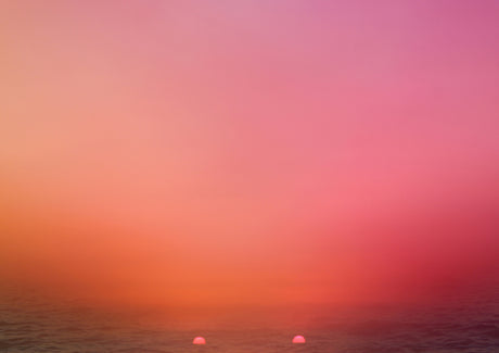 TWO SUNS: This image features a stunning pink and orange sunset over the ocean, with two small, bright suns visible near the horizon. The sky is a vibrant mix of pink, orange, and yellow, creating a beautiful and ethereal effect. The waves are barely visible in the distance, and the overall feel of the image is one of peace and tranquility.