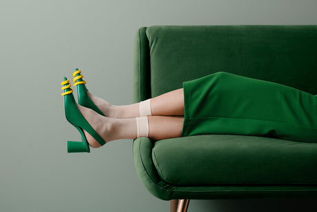 LEMON ZEST: A womans feet, wearing green heels with yellow accents, are resting on a green couch. The woman is wearing white socks and a green skirt, suggesting a comfortable and stylish setting. The image highlights the color green and the relaxed pose of the woman.