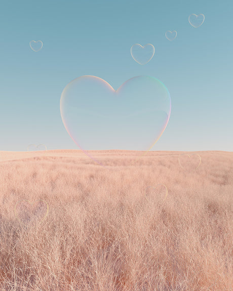 LOVE BUBBLE: A large, heart-shaped bubble floats above a field of tall grass. The bubble casts a faint rainbow as it hovers in the sky. The sky is a bright blue, providing a stark contrast to the soft pink hues of the grass. Several smaller, heart-shaped bubbles appear in the background, adding to the whimsical and romantic feel of the image.