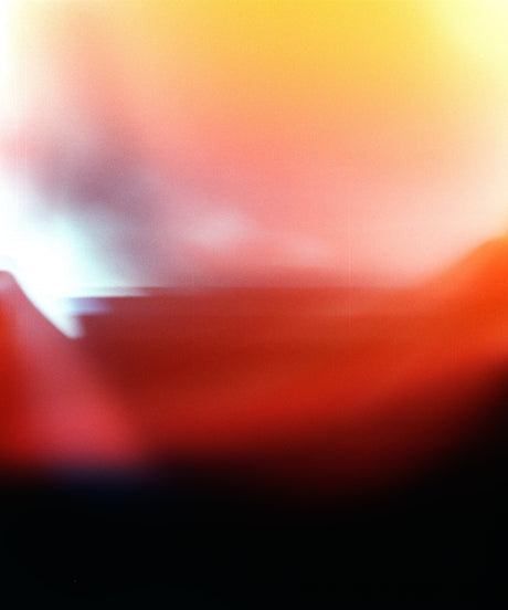 RED: An abstract image of a landscape, with red, yellow, and white hues, taken at sunset. The image is blurred, creating a soft and dreamlike effect. The sky is a mix of warm colors, with a subtle white glow in the top left corner. The bottom of the image is a darker red, transitioning into black at the bottom.