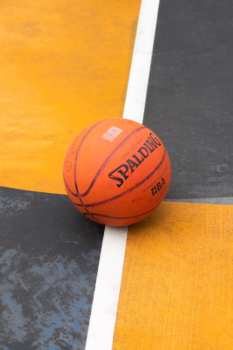 BUMBLEBEE: An orange basketball sits on a black and orange court. The ball is a standard basketball with white lines and the word SPALDING written on it. The ball is slightly tilted to the right.