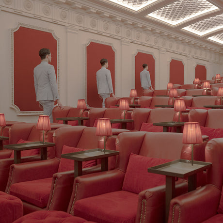 NIGHT AT THE MOVIES 8: This image shows a row of red plush movie theater seats. In the background, three men in suits walk down the aisle towards the screen, which is not visible. The theater is empty with the exception of the men and each seat has a small lamp.