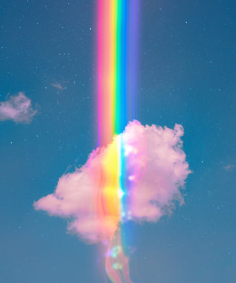 A RIBBON OF DREAMS: A vibrant rainbow shines through a puffy white cloud in a bright blue sky. The sky is dotted with faint white stars. The image captures a moment of ethereal beauty, symbolizing hope and joy.