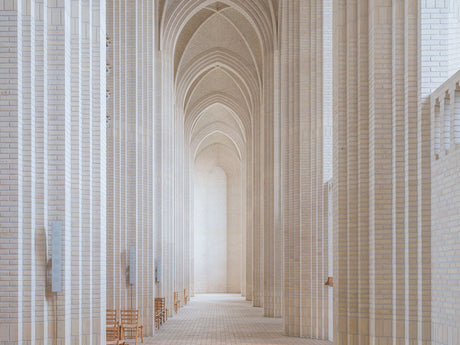 COPENHAGEN CHURCH: A photograph showcasing the interior of a modern church building, featuring a long hallway with white brick columns and arched ceilings. The hallway is illuminated by natural light, creating a sense of serenity and spaciousness. The minimalist architecture emphasizes the simplicity and elegance of the design.