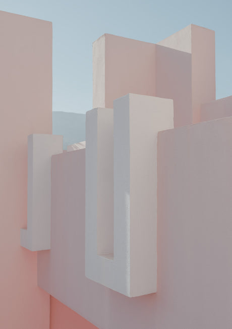 CALPE: A close-up image showcasing the minimalist architectural details of a modern building. White U-shaped elements are embedded within the pink walls, creating a visually striking contrast. The image captures a daytime setting, highlighting the smooth surfaces and clean lines of the building.