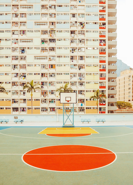 HONG KONG HALF COURT: An empty basketball court in Hong Kong with an orange keyhole and yellow free throw line, situated directly in front of an apartment building with multiple balconies and windows.