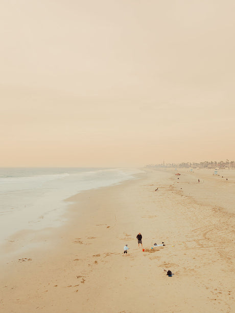 HUNTINGTON BEACH: A family enjoys a day at the beach in California, with the sun setting in the background. The beach is covered in fine sand, and the ocean is calm and serene. The image is taken from a high vantage point, providing a wide view of the beach and ocean.