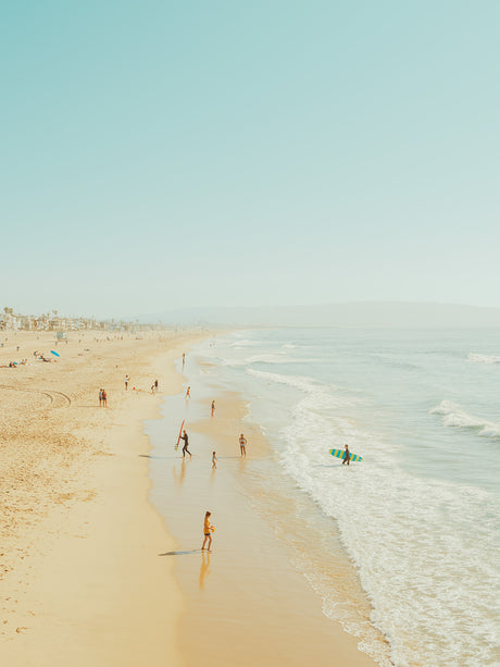 STRIPED SURF: A wide shot of a beach with people enjoying the sunny weather. There are people surfing in the water, walking along the sandy shore, and playing in the waves. The sky is clear and blue, and the ocean is calm and inviting.