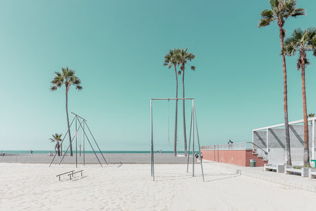 VENICE BEACH GYM: This image shows a sandy beach with palm trees in the background. In the foreground, there is a set of empty exercise equipment, including a pull-up bar and parallel bars. The sky is a bright blue and the sand is white. The overall mood of the image is calm and peaceful.