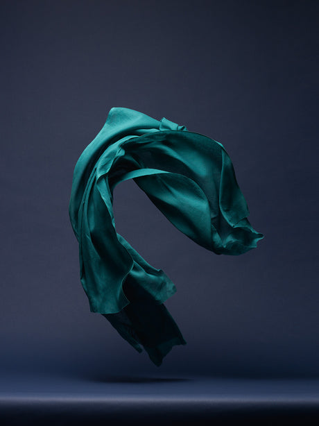 DANCING FABRIC, DARK GREEN ON DARK BLUE: A single piece of teal fabric is suspended in the air, flowing gracefully against a dark blue background. The fabrics smooth texture and elegant movement create a sense of fluidity and motion. The soft lighting illuminates the fabrics vibrant color, highlighting its subtle texture and intricate folds.