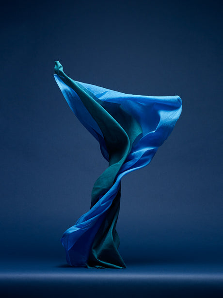 DANCING FABRIC, LIGHT BLUE AND GREEN: This image showcases a blue and green fabric piece flowing and swirling in a studio setting against a deep blue background. The fabrics movement is captured in a dynamic pose, creating a sense of energy and motion.