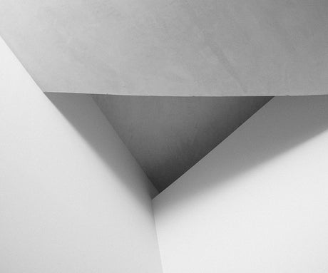 HEART 03: This black and white photograph captures a stark geometric arrangement of interior walls, creating a striking visual composition. The sharp angles and clean lines highlight the minimalist design of the space. The contrasting shades of gray emphasize the interplay of light and shadow.