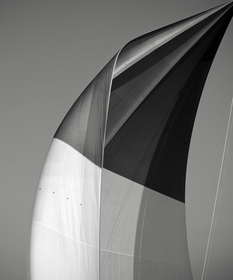 SAILS XX SPINNAKER OF THE VELSHEDA: A black and white image of a close-up detail of a sailboat sail against a grey sky. The sail is filled with wind and is taut and full, showing the intricate patterns and lines of the sail material.