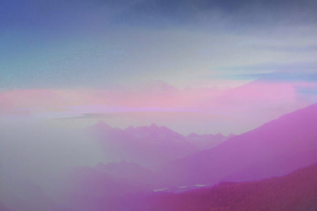 DISSOLUTION I: A panoramic view of a mountain range silhouetted against a vibrant sunset sky, with a soft, pink haze creating a dreamy atmosphere. The distant peaks are shrouded in fog, adding to the ethereal beauty of the scene.