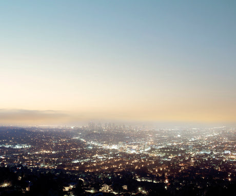 LOS ANGELES, GRIFFITH OBSERVATORY: A panoramic aerial view of the Los Angeles cityscape at twilight. The city lights twinkle below, creating a mesmerizing pattern of urban illumination. The sky is a soft blend of blue and orange, with a hint of haze.