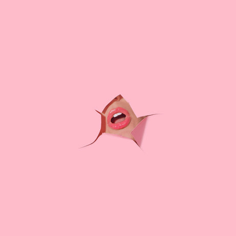 LOVER: A womans mouth with bright pink lipstick is peeking through a torn hole in a pink background. The mouth is open in surprise or excitement, creating a dynamic and visually striking image. The minimalist background allows the focus to be solely on the mouth, making it the central element of the photograph.