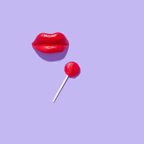 TOTAL SUCKER: A red, molded plastic pair of lips is positioned above a red lollipop on a stick on a lavender background.