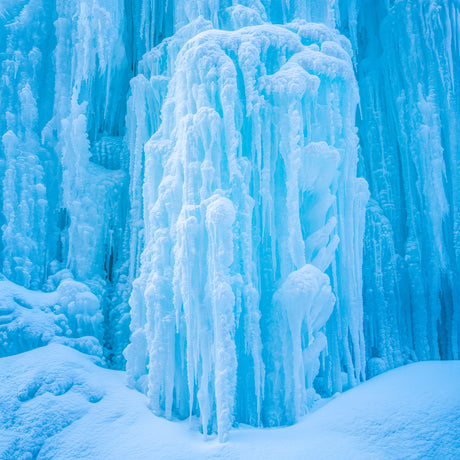 FROZEN WATERFALL III: A close-up photograph of an icy waterfall with a blue hue. The ice formations are tall and narrow, with a smooth, glossy surface. The water is frozen solid, creating a beautiful and unique landscape.