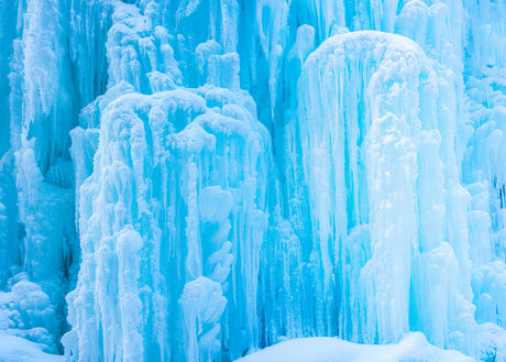 FROZEN WATERFALL II: A close-up photograph of a frozen waterfall, showcasing the intricate formations of blue ice that have formed in the winter. The light reflects off the icy surface, creating a beautiful, ethereal scene.