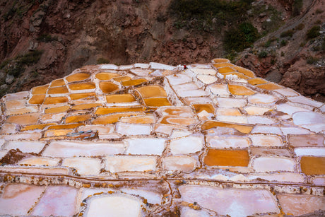 MARAS SALT MINE: A stunning aerial photograph captures the vast Maras salt pans, located in the Sacred Valley of Peru. Thousands of small, rectangular evaporation ponds cascade down a hillside, creating a mesmerizing geometric pattern of white salt and amber-colored brine. The natural beauty of this ancient salt-making technique is evident in this captivating image.