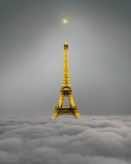 EIFFEL TOWER: The Eiffel Tower, illuminated in a golden glow, rises majestically from a sea of clouds, creating a breathtaking and surreal scene in Paris, France. The towers silhouette is a striking contrast against the soft, gray sky, creating a sense of awe and wonder.