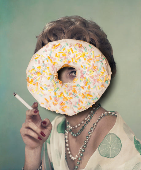 CONSTANT STRUGGLE: A woman with a donut covering her face holds a cigarette. The donut is frosted and covered in colorful sprinkles. She is wearing a white blouse with a green lime print and a pearl necklace.