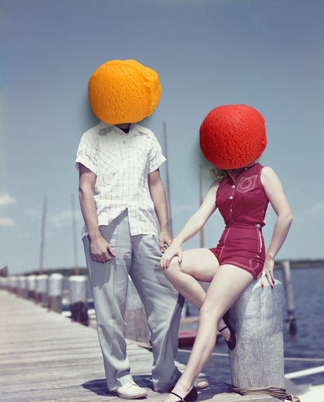 WILL TO BE WEIRD: A vintage photograph showcasing a couple standing on a wooden dock. The man is wearing a plaid shirt and slacks, while the woman is wearing a red one-piece swimsuit. Both individuals have fruit heads, the man a large orange and the woman a large red sphere. The image captures a whimsical and playful scene, with the fruit heads adding a humorous touch to a simple romantic setting.