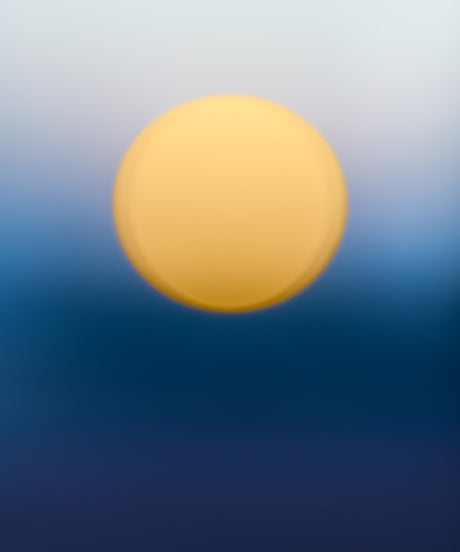 ENDLESS SUMMER NO12: A blurry photo of a sunset. The sun appears as a large, orange circle against a clear, blue sky. The sky is out of focus, giving the image a dream-like quality.