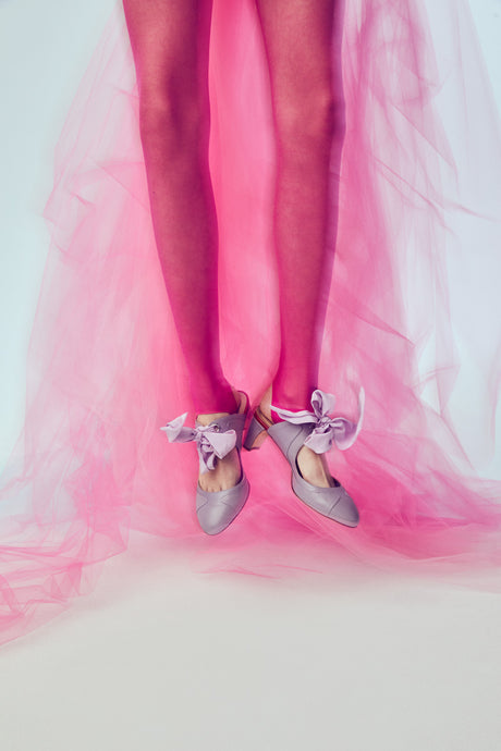 BIRD: This image features a womans legs wearing pink tights and purple shoes with a bow. The shoes are perched on top of a pink tulle fabric, creating a soft and ethereal backdrop. The image evokes a sense of femininity and elegance, capturing the intricate details of the shoes and the flow of the fabric.