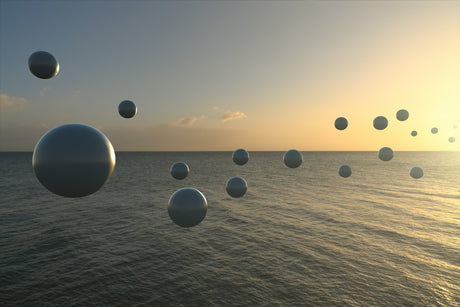 THE BREAKWATER: A photograph of several dark spheres floating in the air above a calm ocean. The sun is setting in the distance, casting a warm glow over the scene. The spheres appear to be suspended in mid-air, creating a sense of mystery and intrigue.