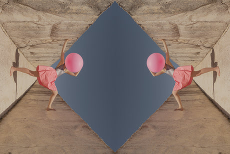 BIG BUBBLE: A mirrored image of a woman holding a large pink balloon against a concrete wall. The woman is in a pink skirt and is walking toward the camera, with her head tilted back and the balloon covering her face. The background is a clear blue sky. The image is a playful and surreal take on everyday objects and environments.