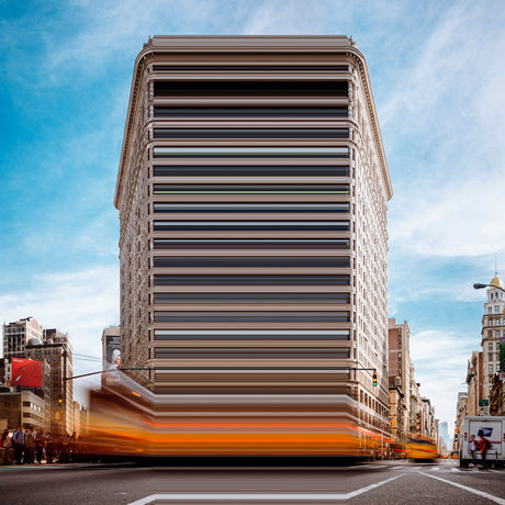 FAT IRON: A tall, brick building with numerous windows, likely an office building, stands tall on a busy city street. The building has a unique design with a striped pattern, and it is surrounded by other buildings and a bustling crowd of people. The street appears busy with traffic, and the sky is bright blue with white clouds, suggesting a daytime setting.