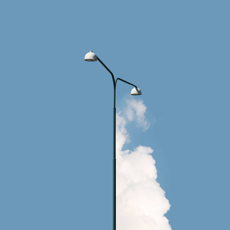 HALF FULL: This image shows a single streetlight post with two lights against a clear blue sky. A puffy white cloud partially obscures the post, creating a surreal and visually interesting contrast. The photograph captures a moment of serenity and tranquility, highlighting the simplicity and beauty of everyday objects.