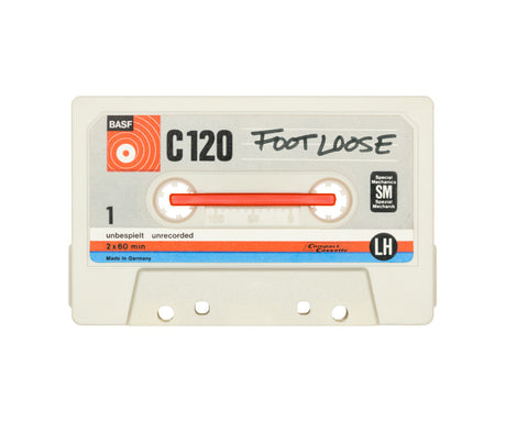 FOOTLOOSE: A close-up shot of a BASF C120 audio cassette tape, labeled Footloose, in a white case. The tape is unrecorded and has a red label on the front. The cassette is made in Germany and features a left-hand