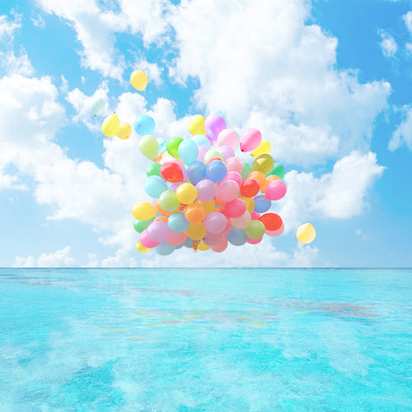 DANCING ON WATER: A large cluster of colorful balloons floats high above a calm, turquoise ocean. The sky is a bright blue with white, fluffy clouds. The balloons are a mix of pastel colors, creating a festive and celebratory atmosphere.