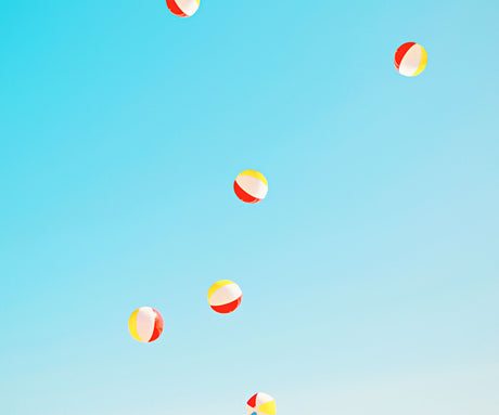 SUMMERTIME: A bright blue sky with six beach balls in various colors floating around. The beach balls are red, yellow, and white, creating a playful and summery scene.