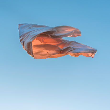 VIENTO 01: A light pink plastic bag is floating in the air, against a clear blue sky. The bag is caught in the wind and billowing out in a graceful, almost elegant way. It is a simple image that captures the beauty of a seemingly mundane object.