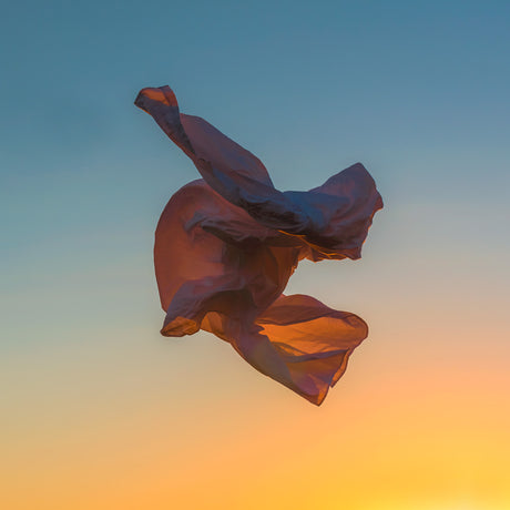 VIENTO 03: A piece of purple fabric floating gracefully in the air against a backdrop of a vibrant sunset. The fabric is caught in a gentle breeze, creating a beautiful sense of movement and fluidity. The warm colors of the sunset create a serene and calming atmosphere.