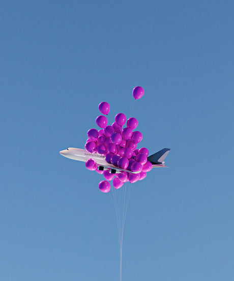 BALLOON FLIGHT 2: A white airplane is lifted by a large cluster of pink balloons in a bright blue sky. The airplane is partially obscured by the balloons. The scene is whimsical and surreal.