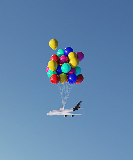 BALLOON FLIGHT 3: A white airplane with black trim is lifted into the air by a large cluster of colorful balloons against a bright blue sky. The balloons are tied to the plane with strings, and the whole scene appears whimsical and lighthearted.