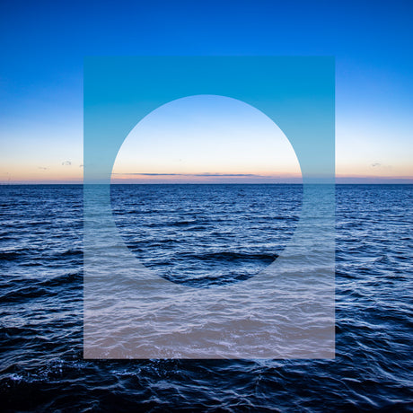 BLUE SEASCAPE: This image features a circular shape overlaid on a photograph of the ocean at sunset. The circle is made of light blue and appears to be floating above the water, creating a sense of depth and perspective. The ocean is a deep blue, and the horizon is a soft pink and orange, indicating the setting sun.