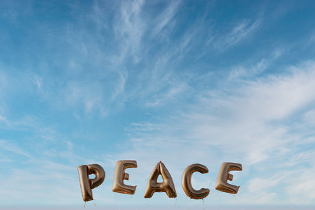 PEACE: A photograph of the word peace spelled out in large golden balloons against a backdrop of a clear blue sky dotted with wispy white clouds. The image evokes a sense of tranquility and hope.